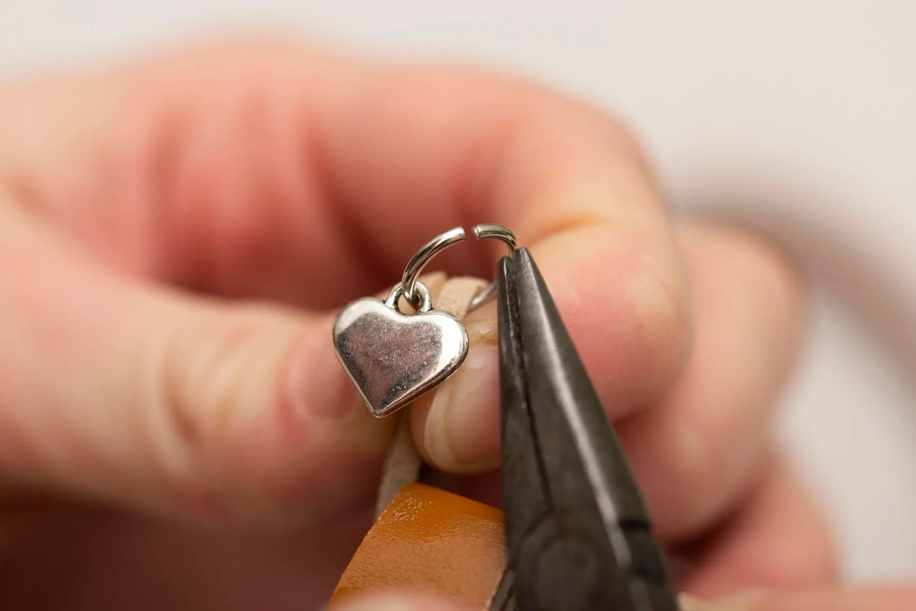 A silver heart charm held in pliers while its jump ring is closed at the repair bench
